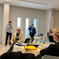 kilka osób w sali konferencyjnej, jedna z nich ma mikrofon przy ustach